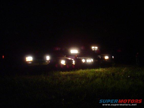 Several SUVs parked at night with their headlights and roof lights on
