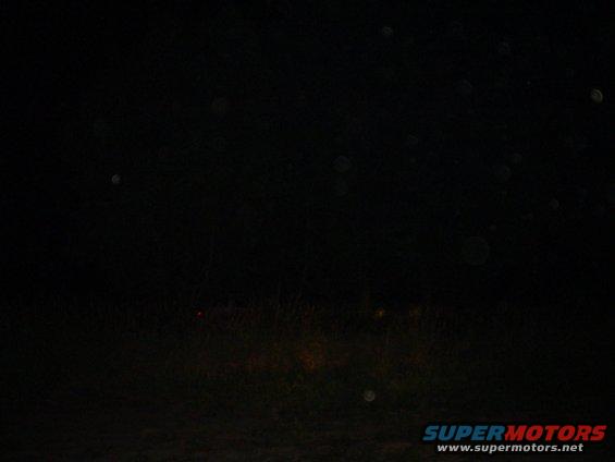Dark scene with faint red and yellow lights visible in the distance, possibly from a vehicle