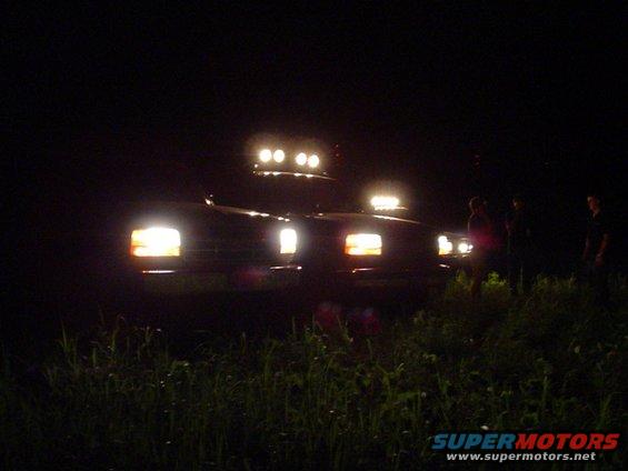 1992 Ford Bronco with light bar and auxiliary lights on, parked at night with people standing nearby