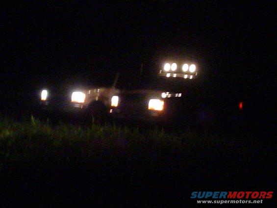 1993 Ford Bronco with four roof-mounted lights and illuminated headlights, seen at night