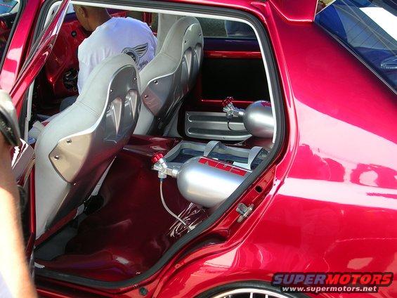 Custom red vehicle interior showing bucket seats and two nitrous oxide tanks mounted on the floor