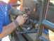 1976 Ford F-100 - Man works on vehicle drivetrain parts, including a driveshaft and U-joint.