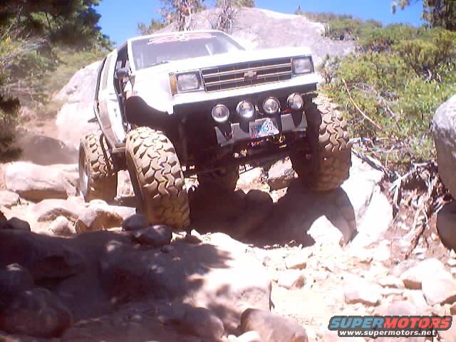 White off-road vehicle with large tires climbing over rocks on a sunny day