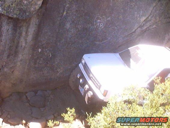 White pickup truck navigating a rocky, off-road trail next to a large boulder
