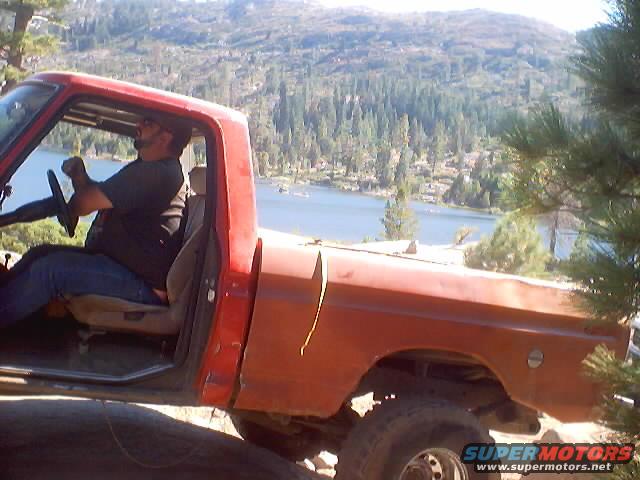 Guy driving an old red pickup truck by a lake