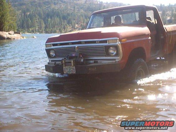 Red pickup truck with winch driving through water; license plate XTC 028