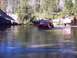 1976 Ford F-100 - Two off-road vehicles navigate a river crossing surrounded by trees and rocky terrain.