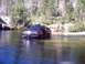 1976 Ford F-100 - A red pickup truck is partially submerged in a river, surrounded by trees and rocky terrain.