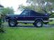 1988 Ford Bronco - Side view of a dark blue 1988 Ford Bronco, a tan stripe and a black soft top.