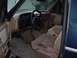 1988 Ford Bronco - The interior of a 1988 Ford Bronco features a tan dashboard and seats, with a prominent steering wheel and gear shift.