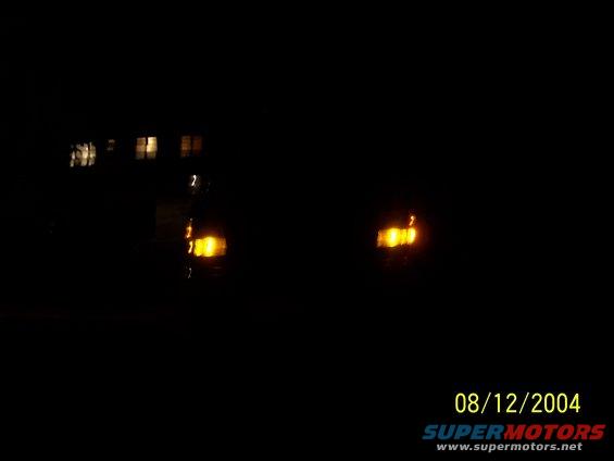 Darkness obscures a vehicle's front end, showing only illuminated headlights and amber turn signals