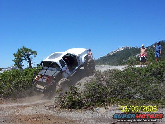 White off-road vehicle with roll cage on a dirt trail, three people standing nearby