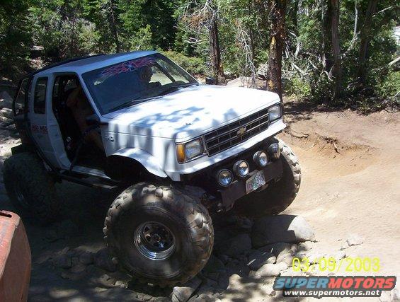 White SUV with large tires on a rocky trail, driver visible inside