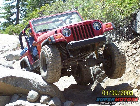 Red Jeep Wrangler navigating a rocky trail, front wheel lifted