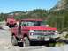 1976 Ford F-100 - Two off-road vehicles, a red Ford F-100 and a red Jeep Wrangler, navigate a rocky mountain path.