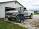 1979 Ford F-150 - A man leans on a lifted 1979 Ford F-150 pickup truck parked in front of a garage.