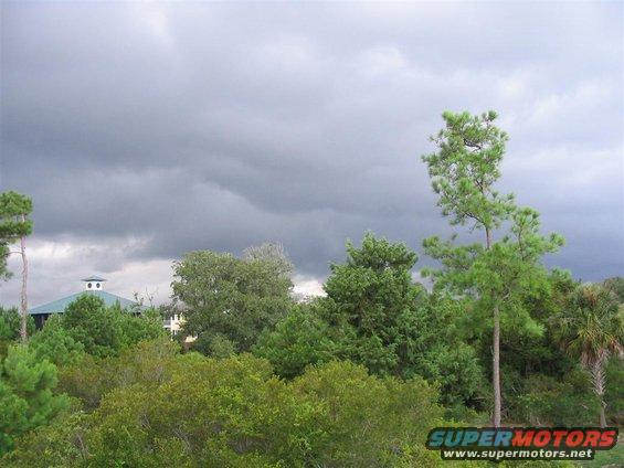 storm clouds gather over a green-roofed building and dense trees