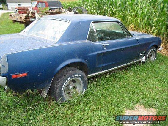Blue 1967 Ford Mustang coupe, rear quarter view, parked in tall grass with cornfield behind