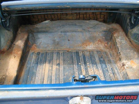Blue car trunk interior with rust and worn upholstery. Ribbed floor and latch mechanism visible