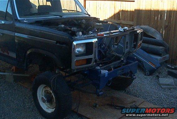 Dark blue pickup truck front end disassembled, showing engine bay and grille removed. Mid-1980s body style