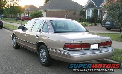 Tan 1995 Ford Crown Victoria parked on street, houses and another vehicle in background