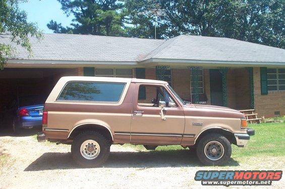 Brown and tan 1987 Ford Bronco parked in front of a brick house, side view