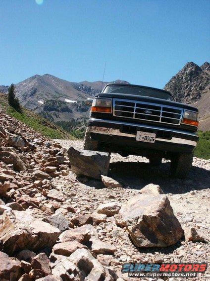 1992 Ford Bronco navigating a steep, rocky mountain trail with large boulders