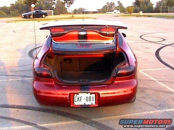 Red coupe with trunk open, racing stripes on the spoiler and trunk lid. License plate EKF 881. Another car in background