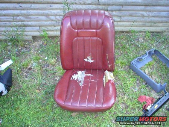 Worn red vinyl car seat with tears, next to a gray plastic trim piece and a seat rail