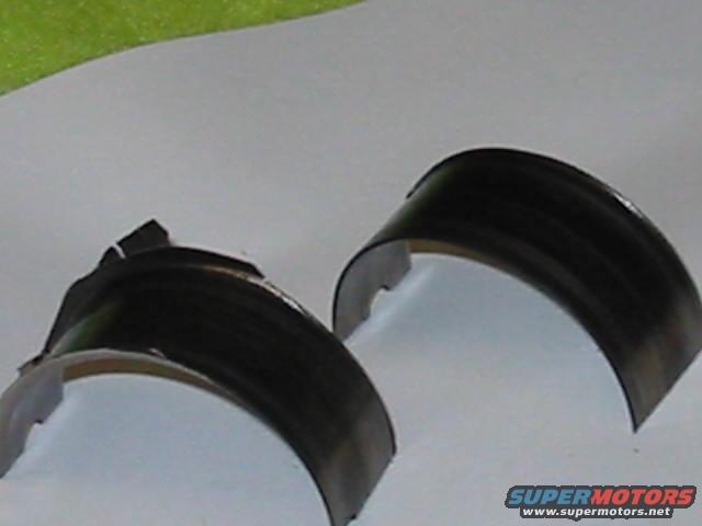 Two engine bearings, one damaged, on a light gray surface