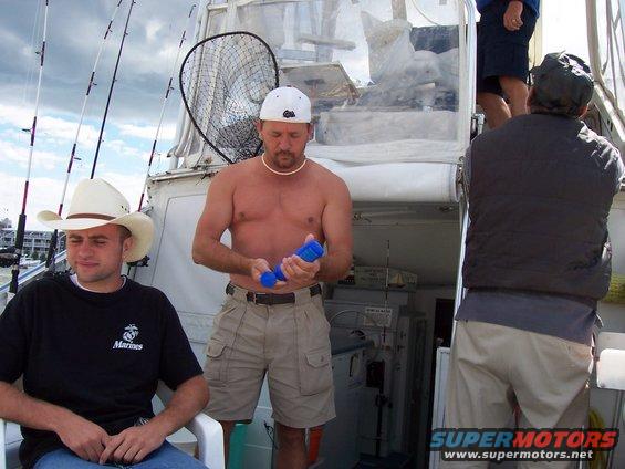 Boat deck with three men, fishing rods, and a net. One man wears a cowboy hat