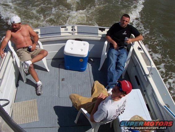 Three men relaxing on a moving boat, one holding a beer