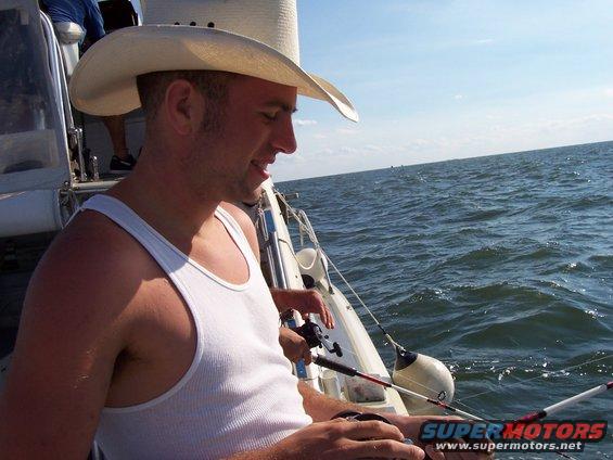 Man in white tank top and cowboy hat fishing from a boat on the water