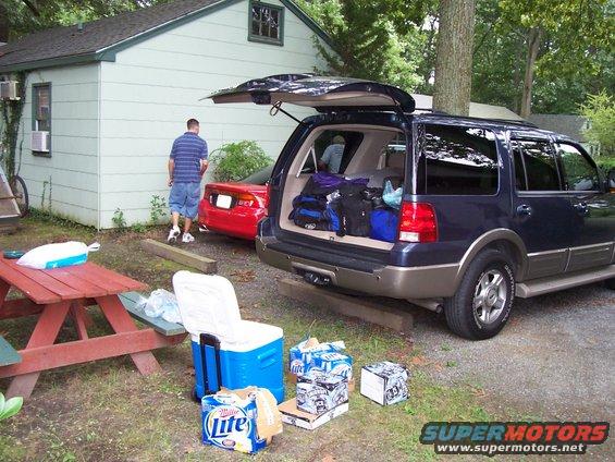 Dark blue SUV with open tailgate loaded with luggage, parked next to a red coupe