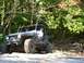1990 Ford Bronco - A person is driving a modified Jeep Wrangler off-road through a wooded area.