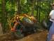 1990 Ford Bronco - An off-road buggy is tilted precariously on a dirt trail surrounded by trees.