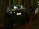 1990 Ford Bronco - Modified off-road vehicle navigating a wooded trail with two people observing.