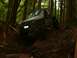 1990 Ford Bronco - This modified off-road vehicle navigates a challenging dirt path through a dense forest.