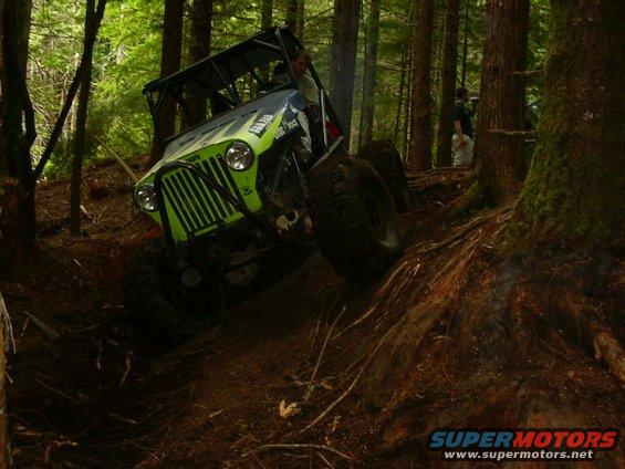 Green off-road vehicle with roll cage climbing a dirt hill in a forest