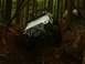1990 Ford Bronco - A white Jeep Wrangler TJ navigates a steep, muddy incline in a dense forest.