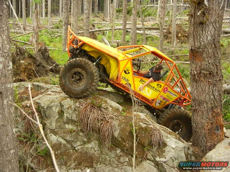 Yellow off-road buggy with roll cage climbing over large rocks in a forest