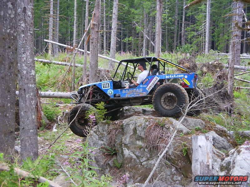 Blue off-road buggy with number 198 on side, climbing over rocks in a forest