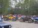 1990 Ford Bronco - A collection of modified off-road vehicles, including a yellow buggy and a red Jeep-style vehicle, are parked together on a gravel surface.