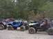 1990 Ford Bronco - Custom off-road buggies are lined up on a dirt surface, with a wooded area behind them.