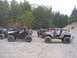 1990 Ford Bronco - A group of off-road vehicles are gathered in a wooded area, with some people standing around them.