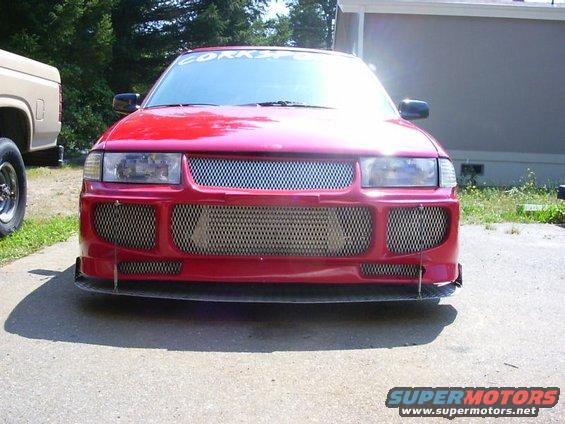 Red car with custom mesh grille and front splitter, parked next to a tan pickup truck