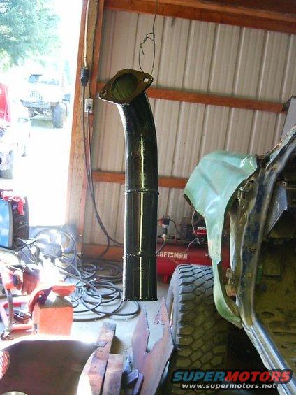 Exhaust pipe hanging from ceiling in garage, next to a vehicle under repair. Air compressor visible