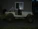 1990 Ford Bronco - This muddy white Jeep CJ is seen from the side, a roll cage and off-road tires.