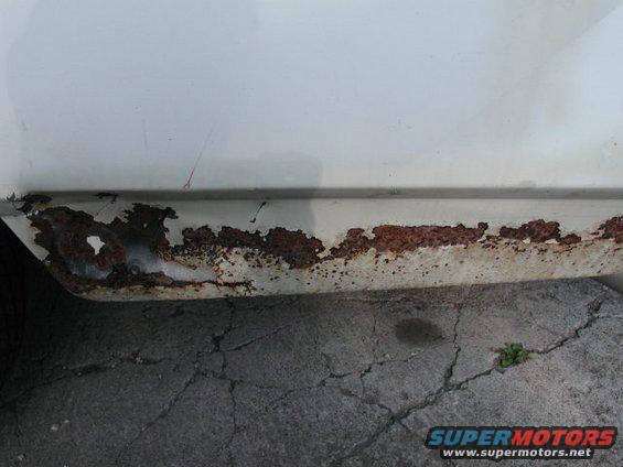 White car rocker panel with extensive rust damage and peeling paint