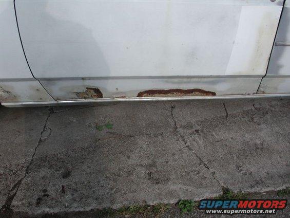 White car door with rust damage on the lower panel and trim